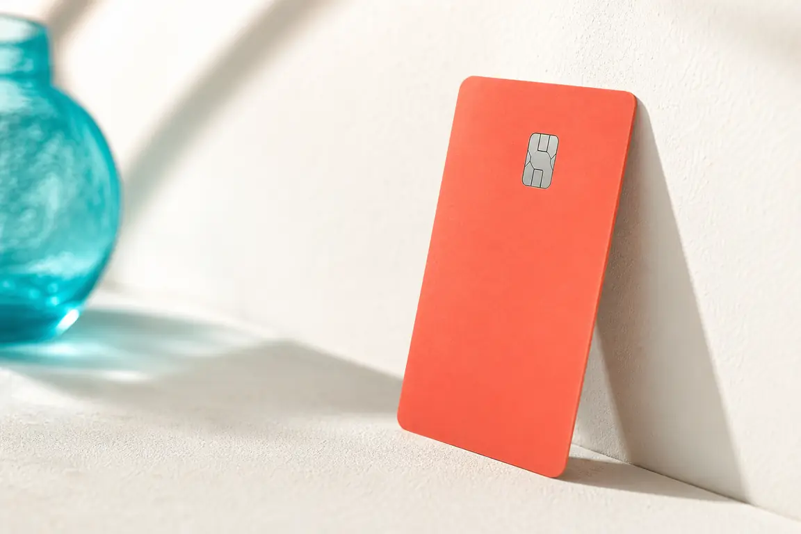 A plain coral bank card standing on its edge against a pale wall.