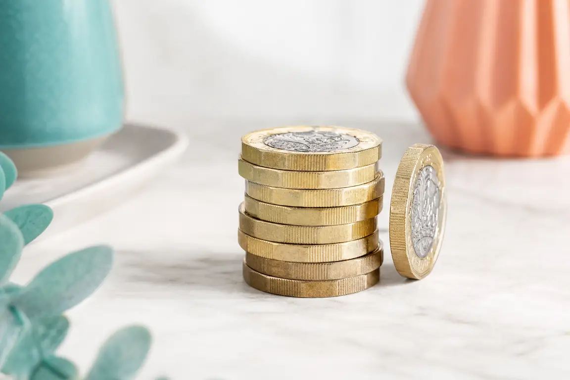 A neat stack of pound coins with one coin standing on its edge beside it.