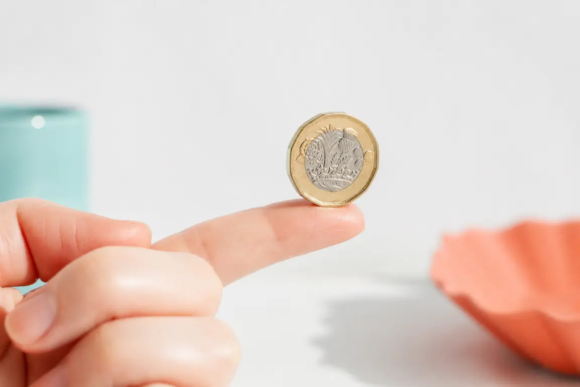 A single pound coin balanced on a fingertip.