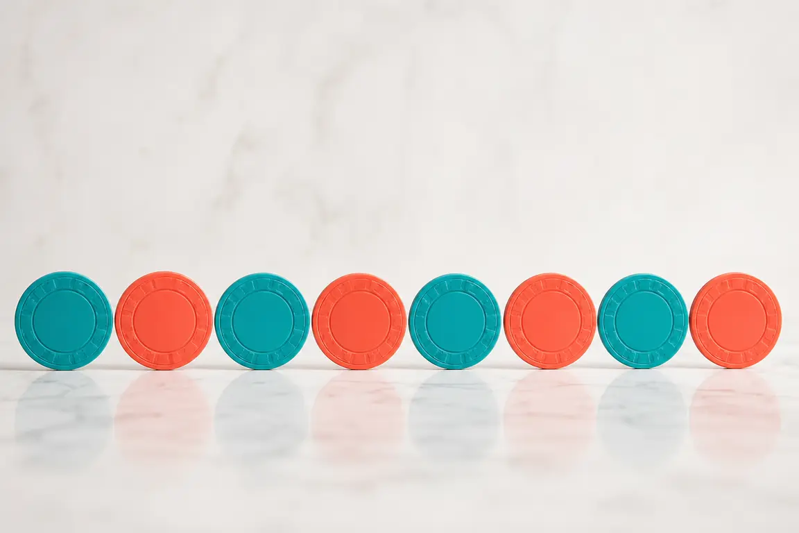 Eight plain casino gaming tokens laid out in a neat row, some turquoise and some coral.