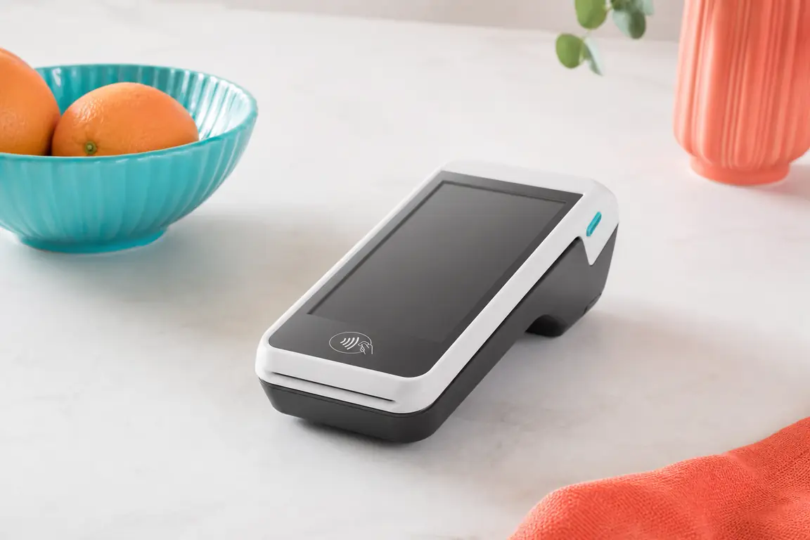 A plain contactless payment terminal on a pale desk, blank screen.