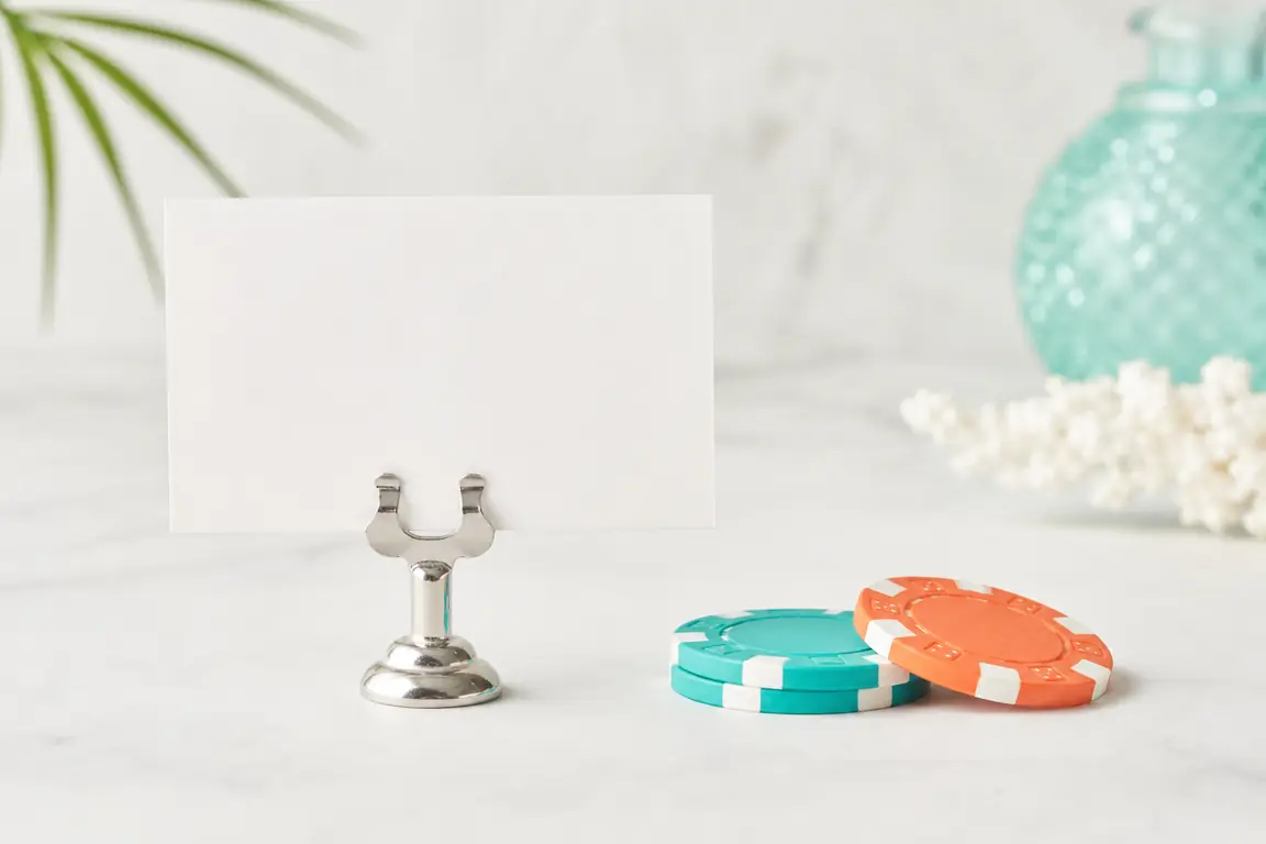 A small blank printed card held in a metal clip, standing beside two casino gaming tokens.